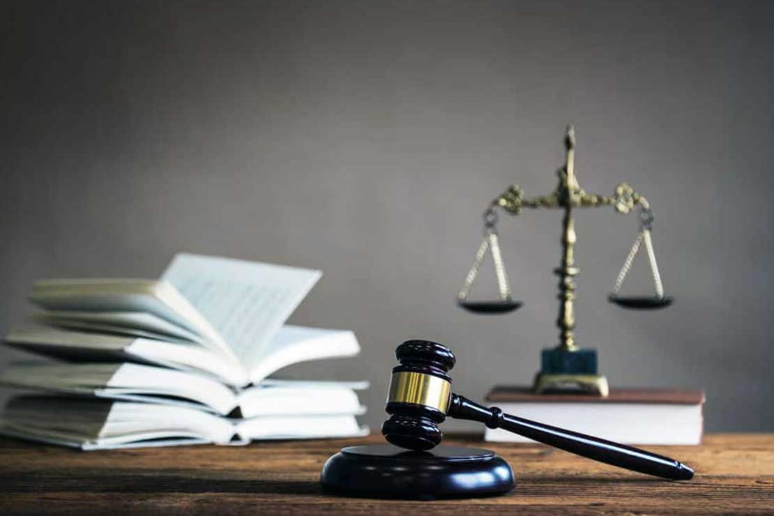 Ξύλινο σφυρί σε πρώτο πλάνο και στο βάθος μια μεταλλική ζυγαριά και ανοιχτά βιβλία